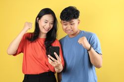 Young Indonesian Couple Look at Mobile Phone and Gesturing Win, Clenched Fist.
