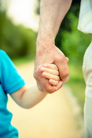 Child holding hand of older man outside in park