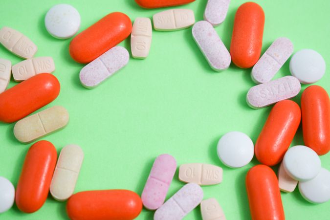 Pills and vitamins framing green background