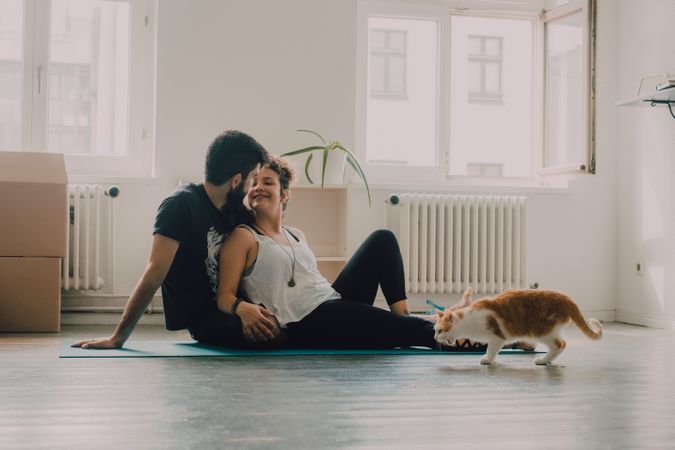 Loving couple cuddling on floor while cat walking around