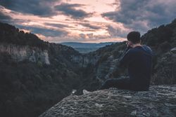 man with photo camera sitting on hill mountain with magnificent sunset
