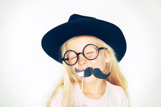 Blonde girl with eyes closed wearing hat, glasses and fake mustache
