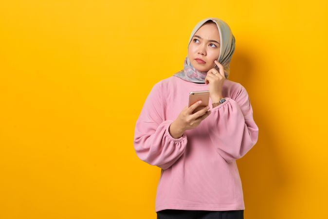 Muslim woman in headscarf contemplating something while holding smart phone