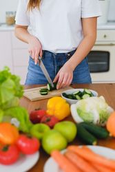 Cropped image of woman slicing a cucumber on brown wooden chopping board 0WLjP5