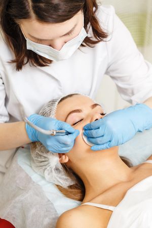 Woman having facial beauty treatment with machine on her forehead, vertical