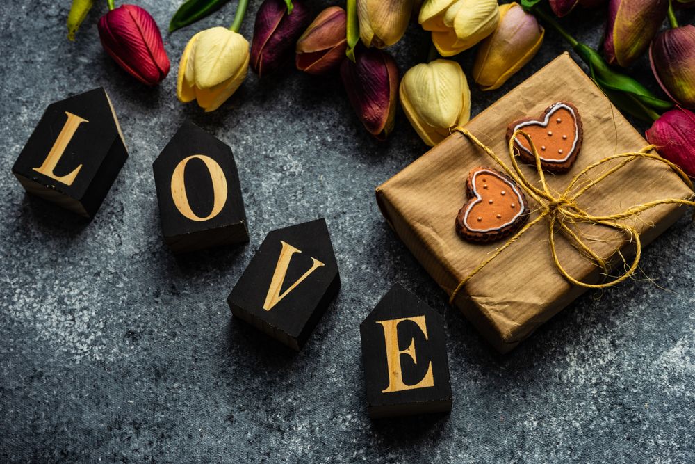 Valentine's day card concept with the word "love" on grey counter with spring flowers, heart ornaments and gift