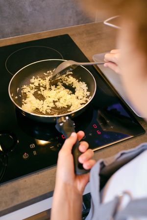 Crop person stirring chopped onion in pan on stove