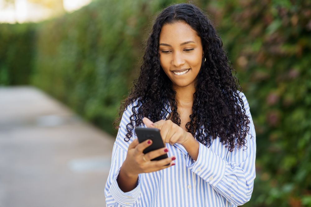 A young woman happily engages with her smartphone in the outdoors, surrounded by nature