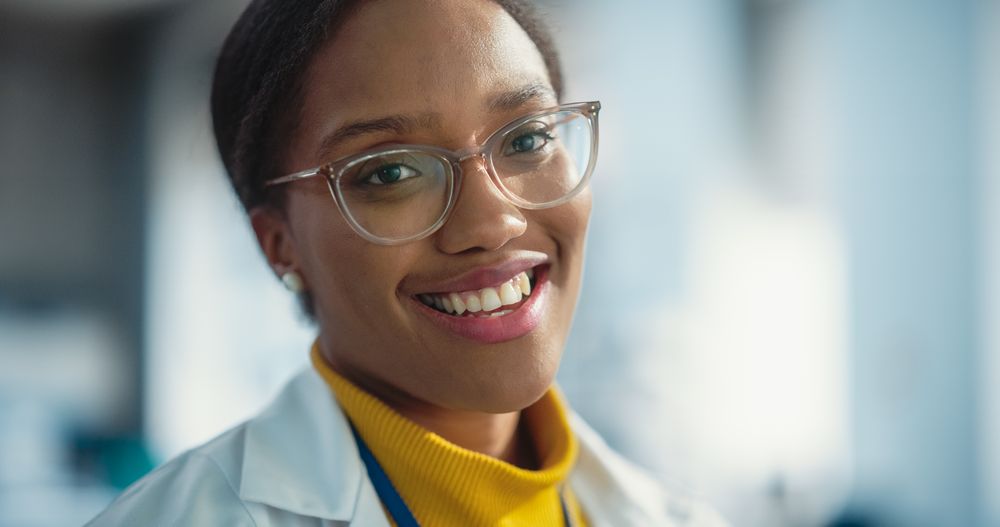 Portrait of Smiling Black Woman Wearing Glasses and Lab Coat Looking at the Camera.