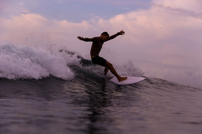 Man on surf board on waving water at sunset