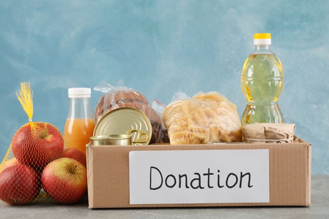 Donation box with different food on gray table. Volunteering