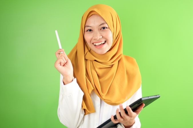 Asian Hijab Woman Holding Tab and Pen, Smiling at the Camera