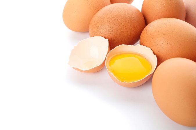 Chicken eggs and half broken egg with yolk  isolated on light background, closeup