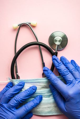 Top view of pink table with hands holding facemask & stethoscope