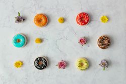 Border of colorful donuts and flowers on marble background