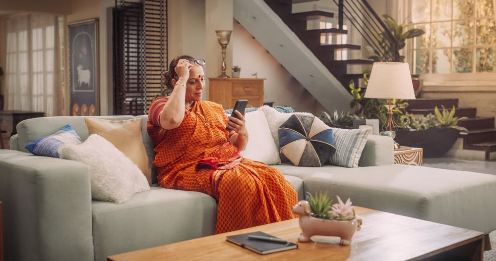 Mature Hindu Woman Using Smartphone at Home: Talking with Loved Ones through Video Calls, Reading News Article Online and Watching Videos