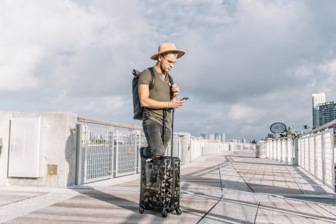 Young man traveling with suitcase and using his smartphone.