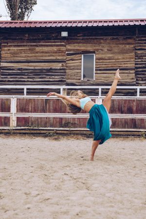 Flexible woman in colorful skirt dancing at rural paddock