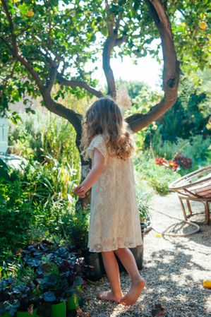 Young girl  in dress explores garden facing away from the camera