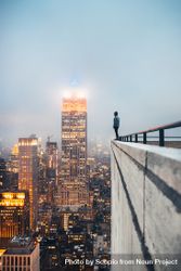 Man in dark jacket standing on the edge of a high rise building in city 4Mvzyb