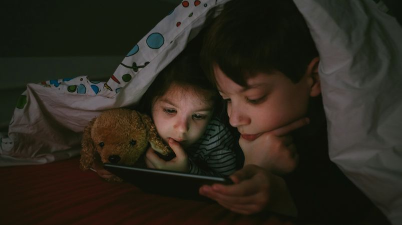 Siblings looking at the tablet in the dark