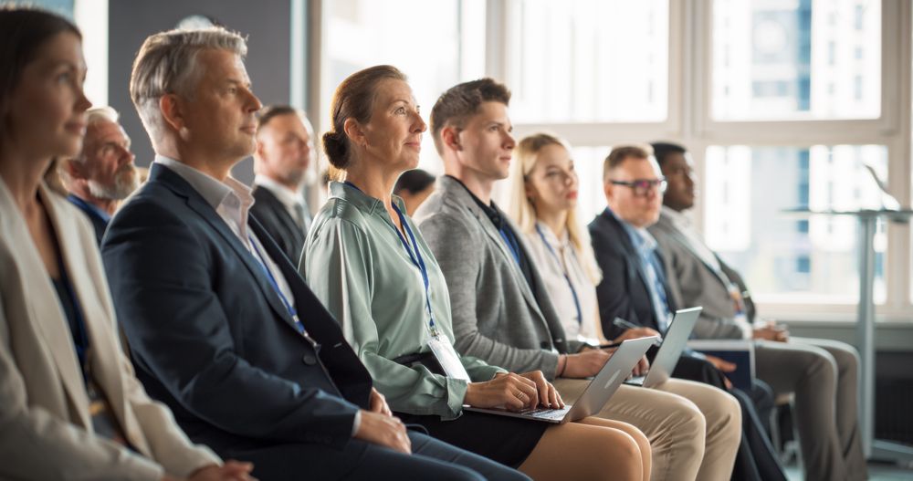 Woman Sitting in Crowded Audience at a Business Conference. Female Top Manager Smiling, Using Laptop Computer.