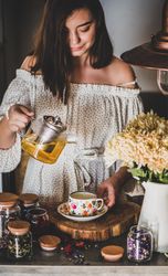 Woman pouring tea in floral cup and saucer from glass teapot