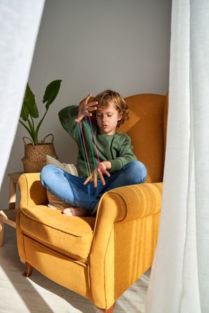 Boy stretching colorful strings in armchair