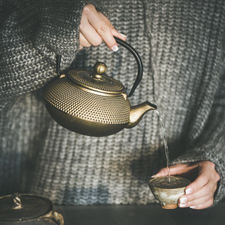 Woman in cozy sweater pouring from traditional Japanese tea set, square crop