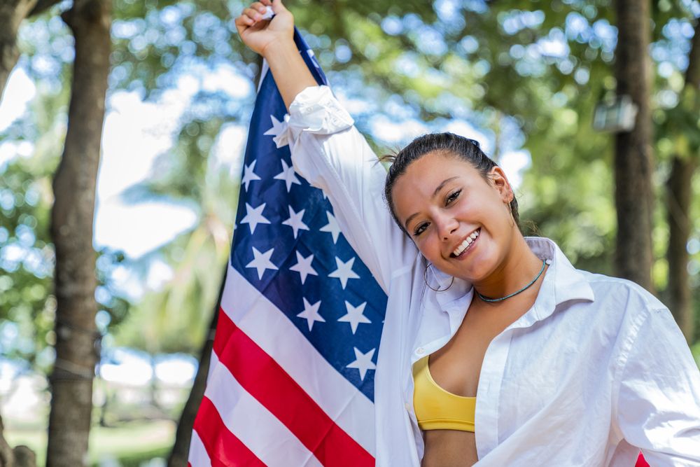 Content woman smiling wrapped in American flag walking along park