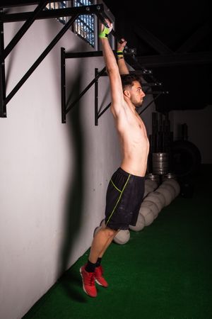 Man hanging on bar near wall in gym