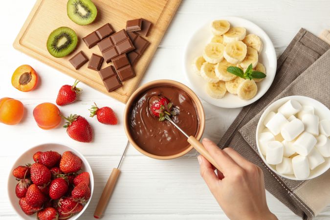 Woman dipping strawberry in chocolate. Delicious chocolate fondue