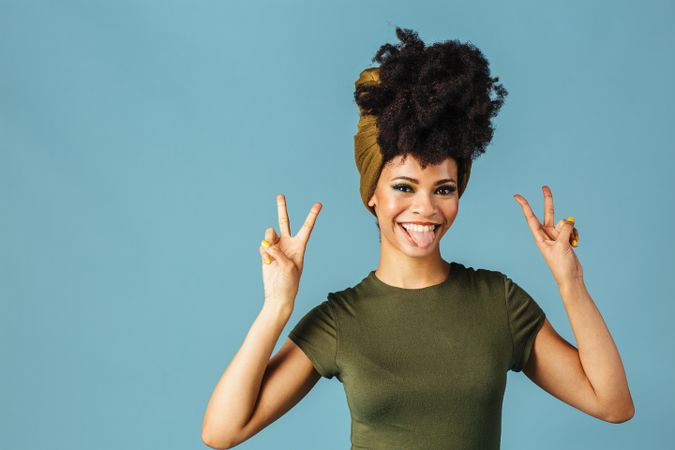 Studio shoot of Black woman smiling making the peace sign with her tongue out