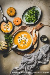 Two bowls of pumpkin soup with garnishes, bread, cream, squash, on concrete surface begmp5