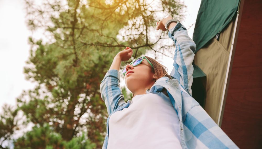 Woman with sunglasses stretching her arms over nature background