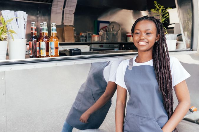 Smiling Black woman in apron outside her food truck window