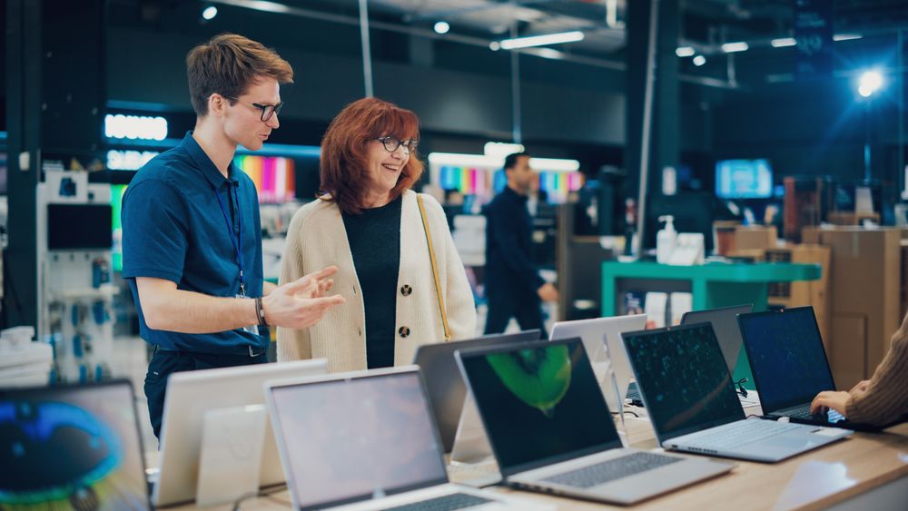 Woman Having a Conversation with a Salesperson in Home Electronics Store while Selecting a Laptop.