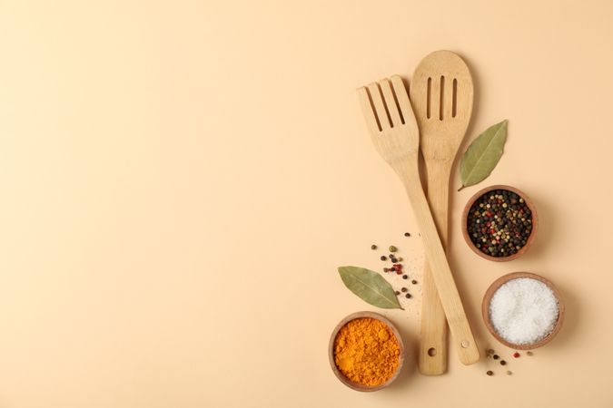 Wooden kitchen cutlery and spices on beige background, space for text