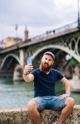 Satisfied male tourist taking selfie on smartphone at quay