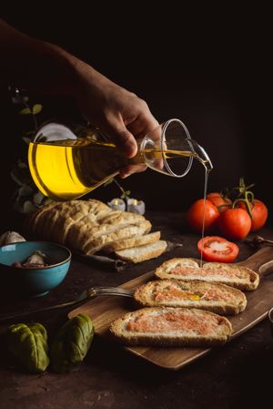 Crop person pouring oil on toasts