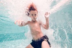 Funny boy swimming underwater in pool