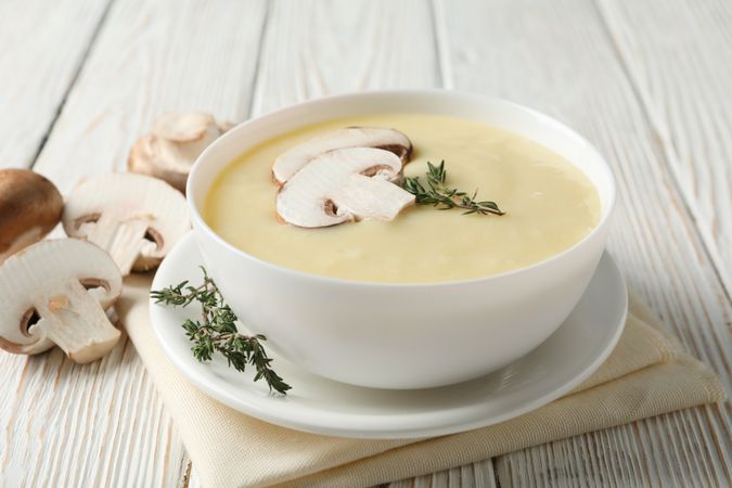 Close up of bowl of creamy mushroom soup with herbs on napkin on wooden table