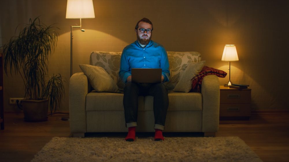 Portrait Shot of a Man Sitting on a Couch in His Living Room, Laptop on His Knees. He's Working.