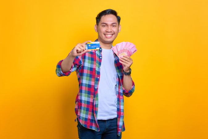 Smiling Asian man holding credit card and cash in studio shoot