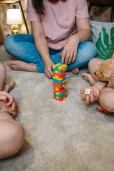 Unrecognizable family having fun making a tower with wooden stacking piece game over carpet at home