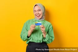 Muslim woman in headscarf and green blouse winking while holding credit card 0K1dD4