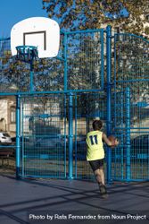 Teenager playing basketball on an outdoors court 56jnL5