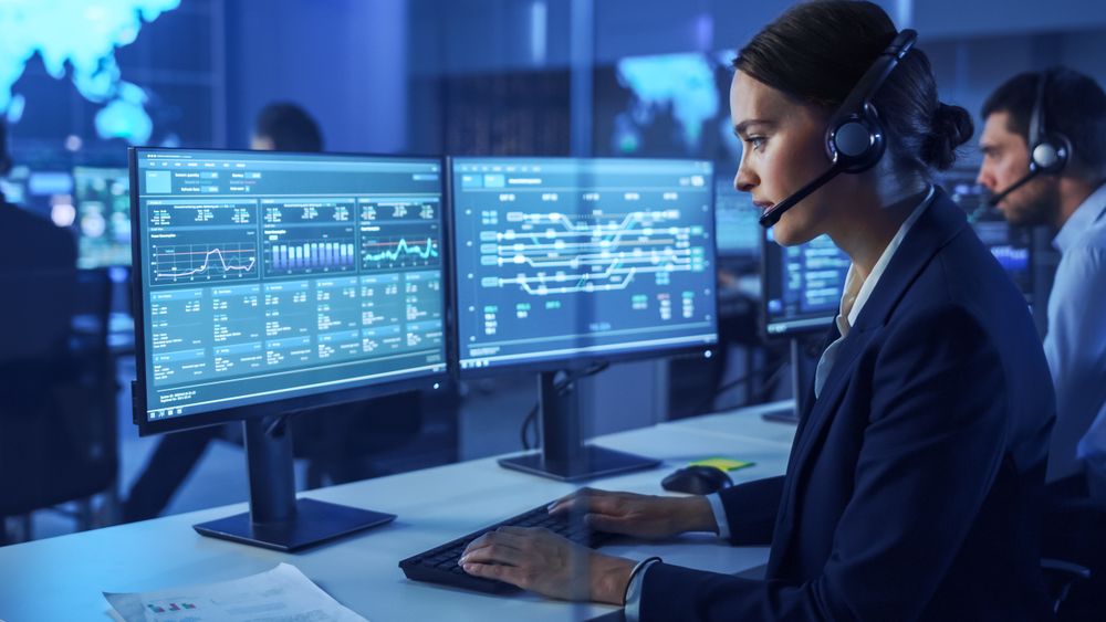 Customer Support Agent Analyzes Data on Multiple Screens in Blue-lit Operations Center.