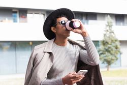 Stylish hispanic man with smartphone and coffee to go outdoors