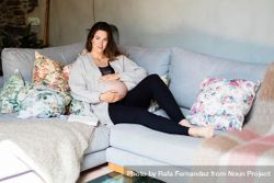 Relaxed pregnant woman holding her belly on sofa 4djPQ0